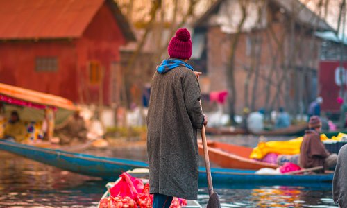 A man in a hat skillfully maneuvers a boat across the tranquil water surface.