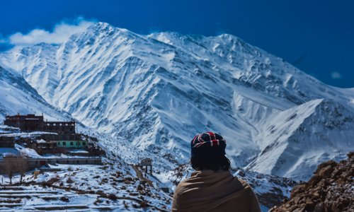 A man wrapped in a blanket gazes at the majestic mountains in the distance.